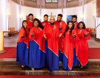 9 Gospelsängerinnen und -Sänger in rot-blauen Roben in silbernen Details